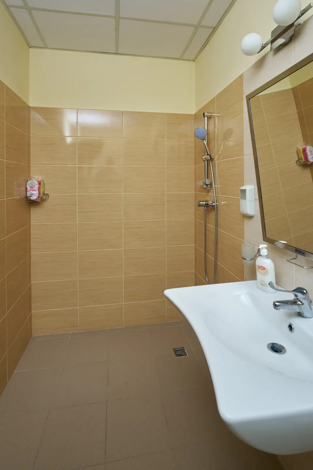 Baie modernă cu gresie bej, duș cu cap reglabil, lavoar alb și săpun lichid, AsertivO Otopeni
