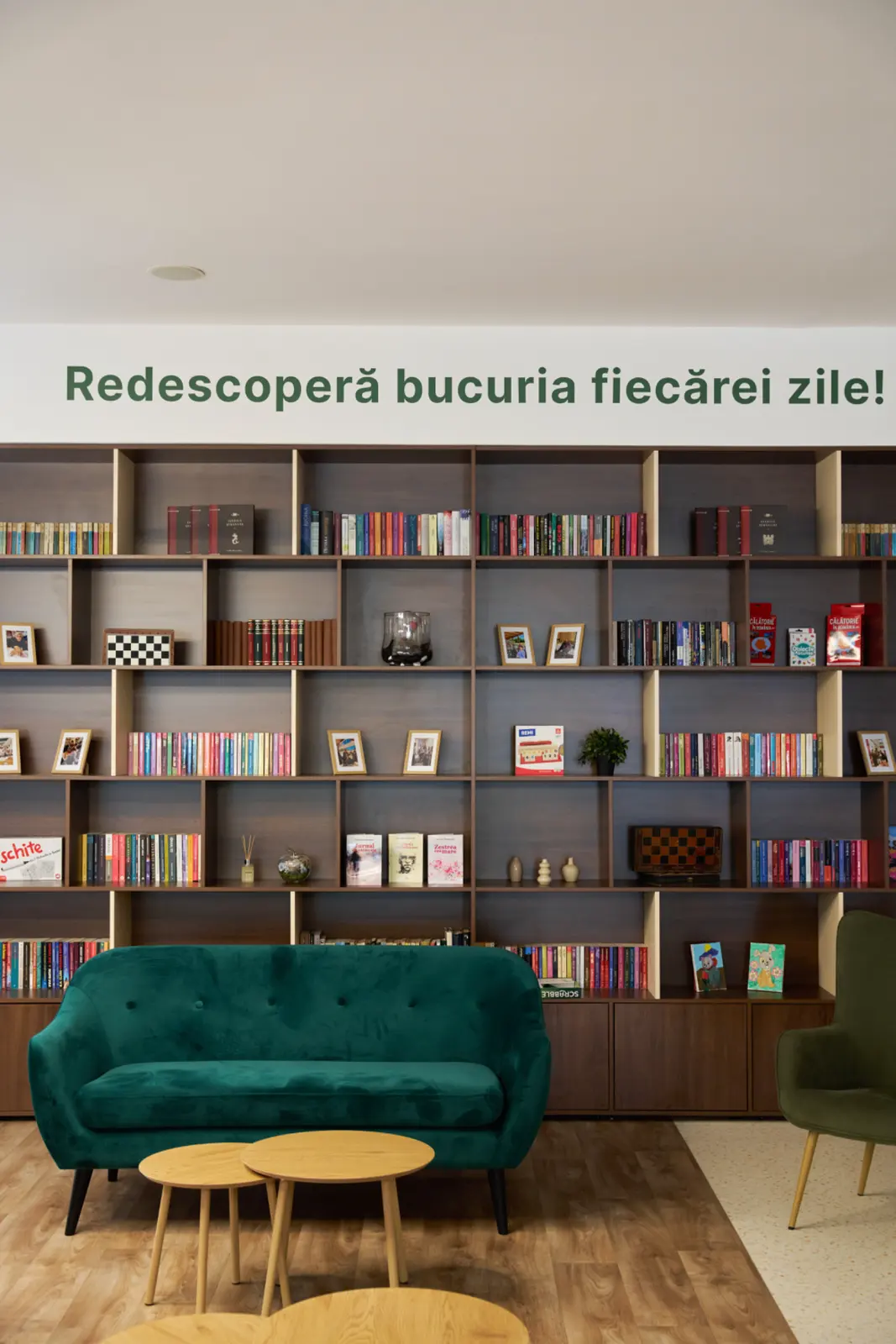 Bibliotecă cu rafturi pline de cărți, canapea verde din catifea, AsertivO Otopeni