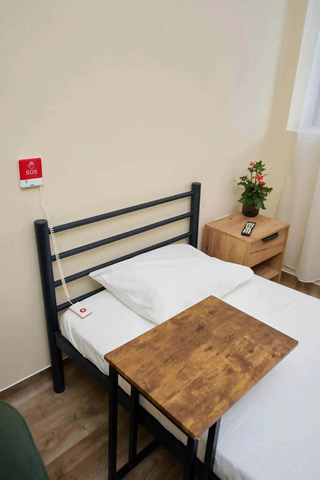Cameră individuală pentru seniori cu saltea metalic negru, lenjerie albă, buton de urgență SOS pe perete, AsertivO Otopeni