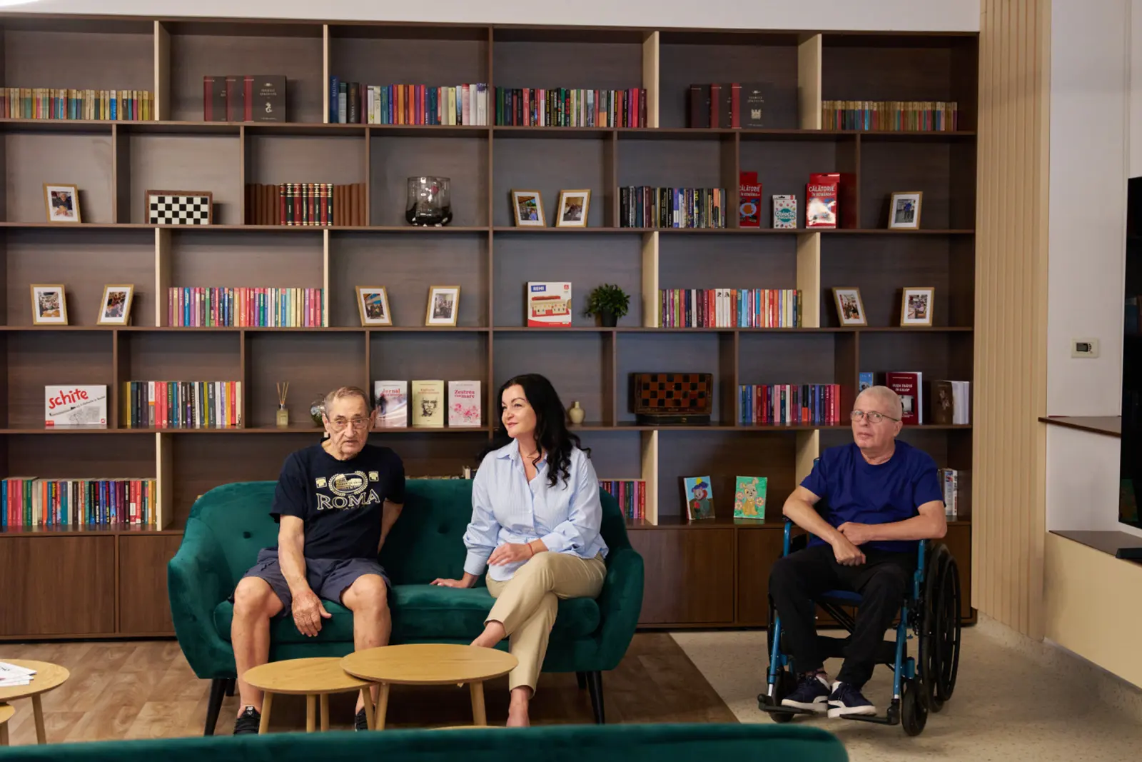 Doi seniori și o îngrijitoare stând pe o canapea verde într-o sală de relaxare modernă, AsertivO Otopeni