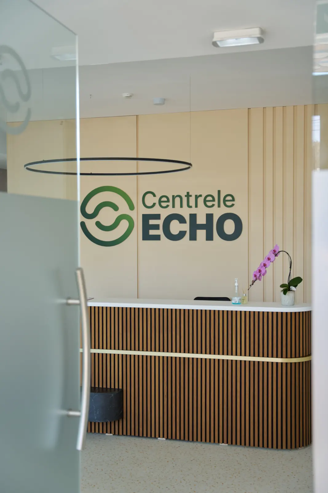 Recepția Centrelor Echo cu logo verde pe perete, tejghea din lemn cu dungi verticale, AsertivO Otopeni
