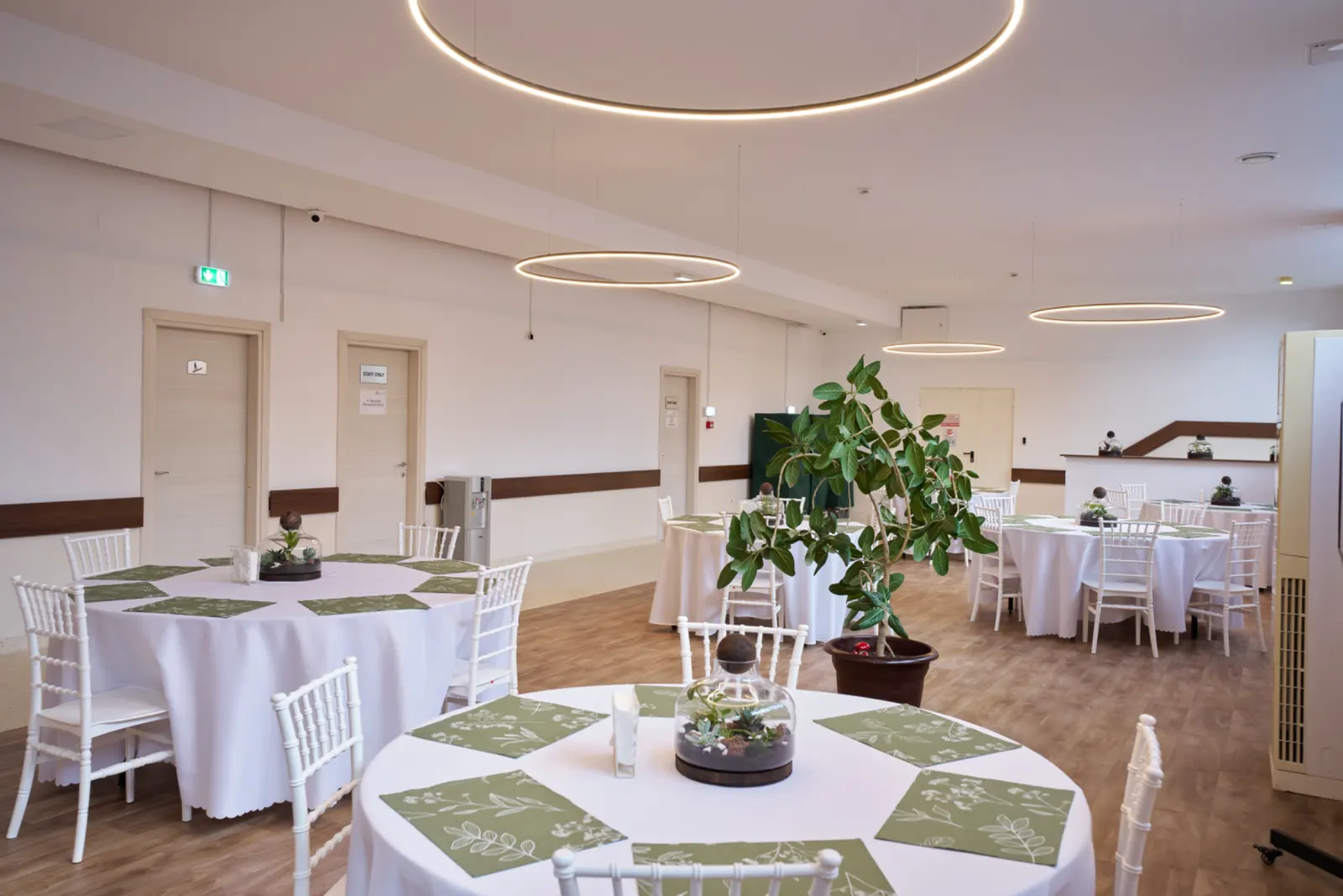 Sală de evenimente amenajată elegant cu mese rotunde acoperite cu fețe de masă albe, scaune Chiavari albe, AsertivO Otopeni