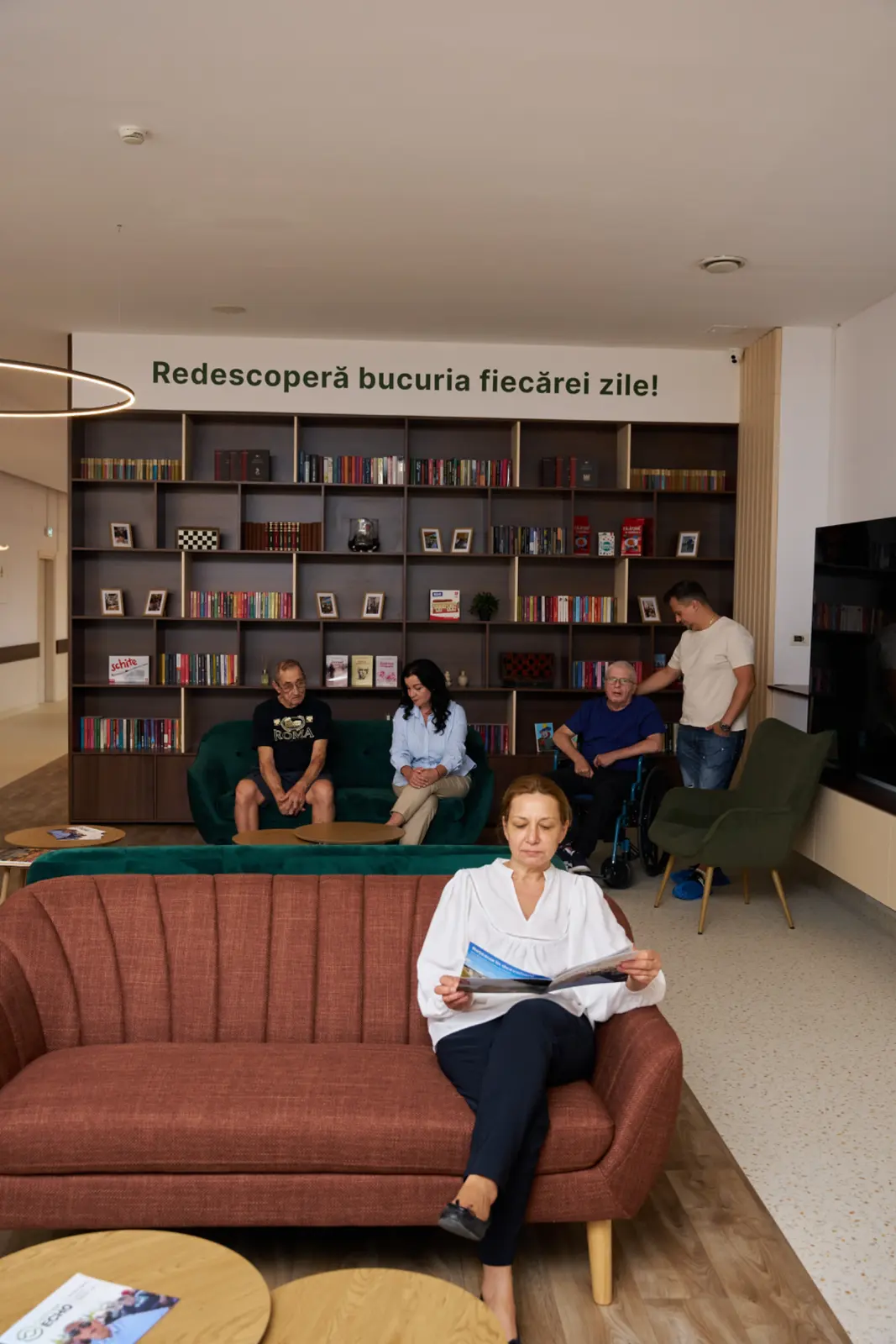 Seniori și îngrijitori în sala de zi a unui centru rezidențial din România, cu canapele colorate, AsertivO Otopeni