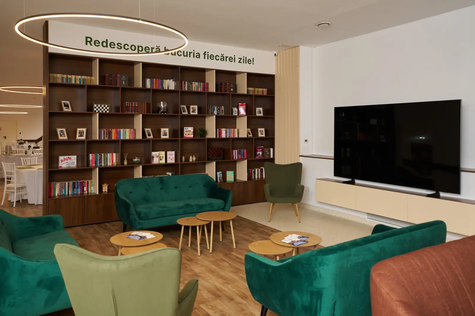 Spațiu de lectură luminos cu bibliotecă din lemn plină de cărți, canapele și fotolii de catifea verde, AsertivO Otopeni