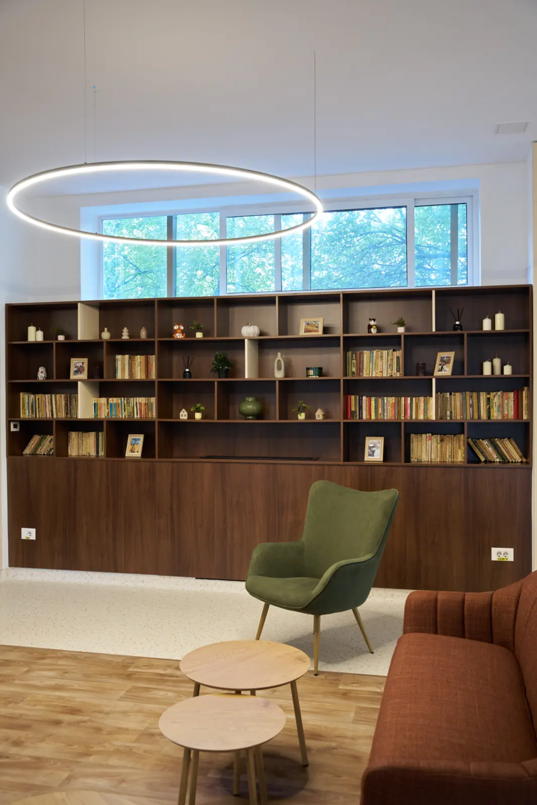 Zonă de lectură și relaxare cu bibliotecă mare din lemn întunecat, fotoliu verde, canapea teracotă, AsertivO Otopeni