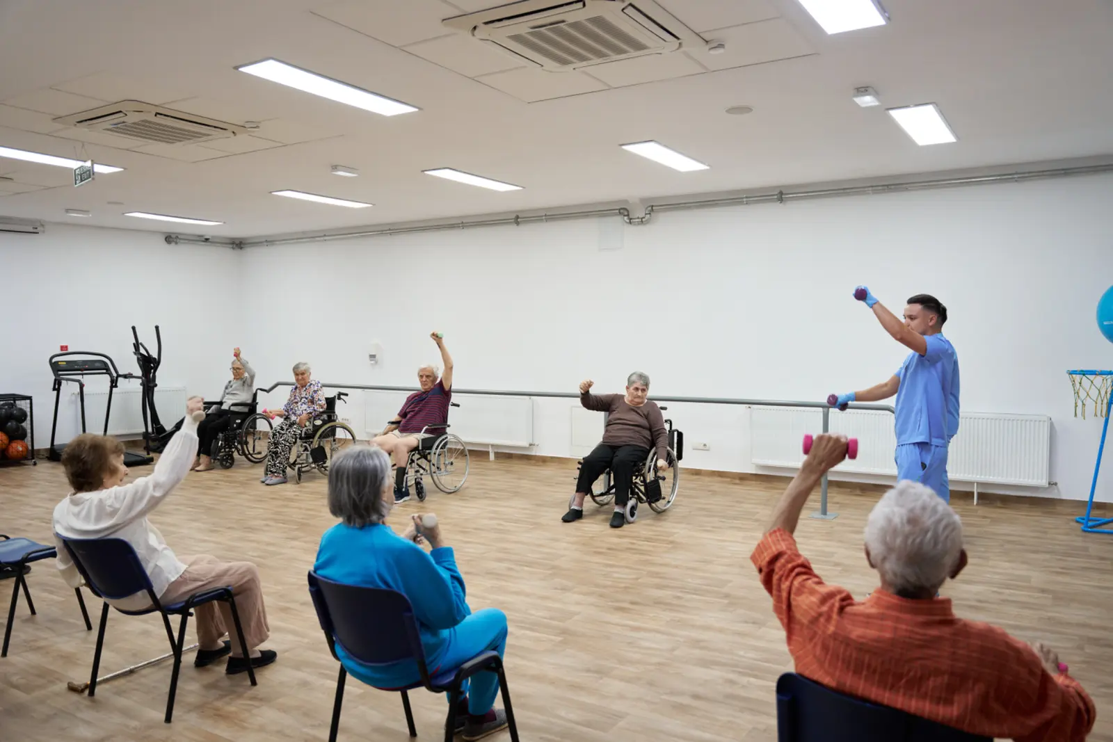 Grup de seniori participând la exerciții de kinetoterapie cu haltere mici, unii în scaune cu rotile, AsertivO Otopeni