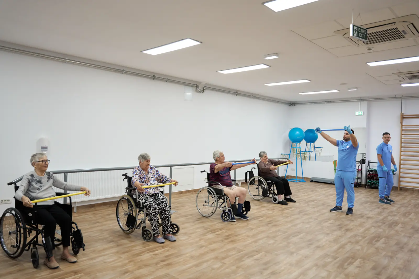 Patru senioare în scaune rulante efectuează exerciții de kinetoterapie cu bastoane și benzi elastice, AsertivO Otopeni